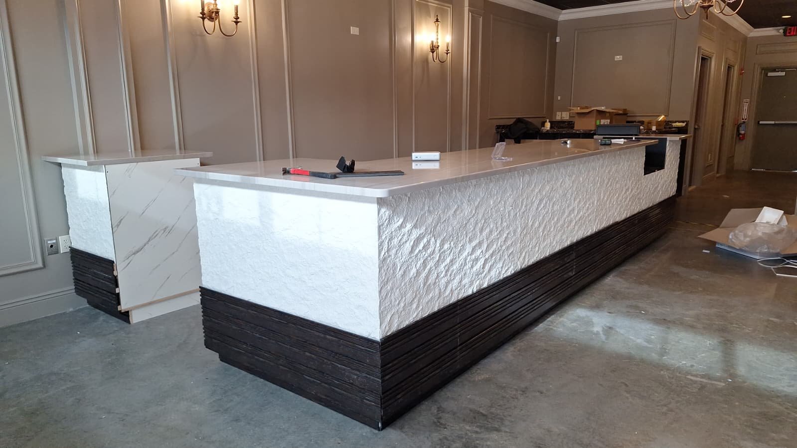 Long reception counter with textured white cladding and dark trim during fit-out
