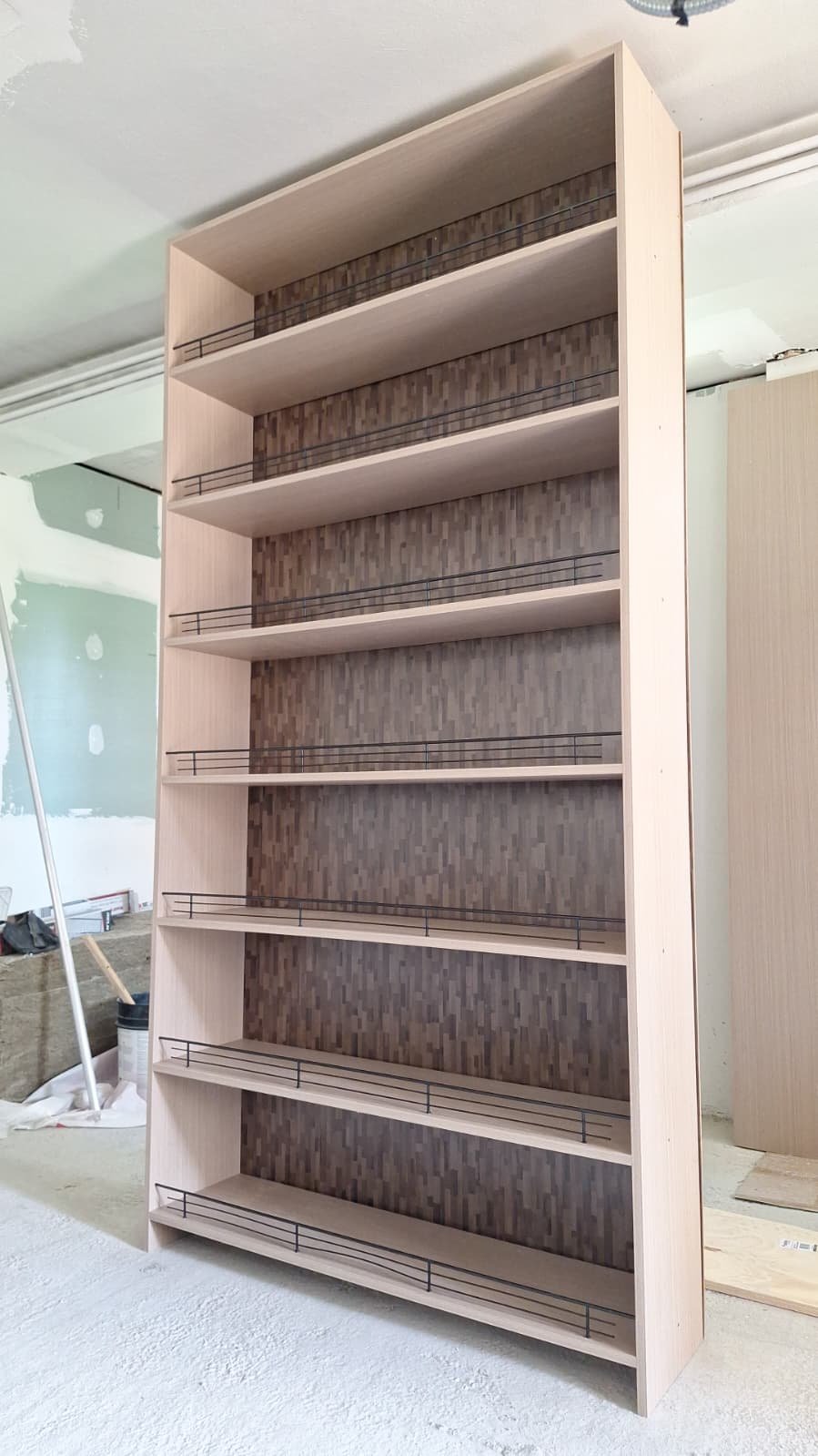 Tall light wood-look shelving with patterned backing and black shelf rails